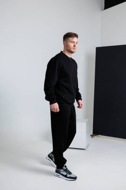 Şık ve şık bir adam basit bir minimalist geçmişe karşı gösterişli siyah spor kıyafetleri modelliyor.