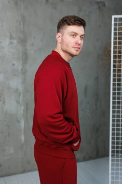Modayı takip eden genç bir adam, çağdaş tarzını ve çekiciliğini sergileyerek, kendine güvenen kırmızı bir kıyafet içinde poz veriyor.