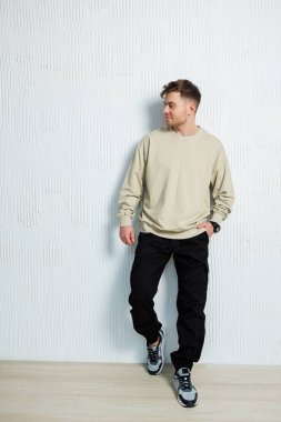 Modayı takip eden genç bir adam şık ama şık giysiler içinde şık desenli bir duvar yüzeyine karşı duruyor.