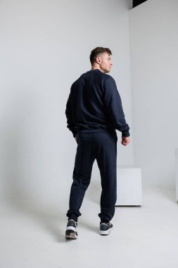 Bir adam gururla modern, şık bir stüdyo ortamında modaya uygun ve şık bir koyu renk spor kıyafeti sergiliyor.