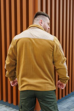 Arkadan görülen şık bir adam, modaya uygun bir ceket giymiş, çarpıcı bir modern mimari zemin hazırlıyor.