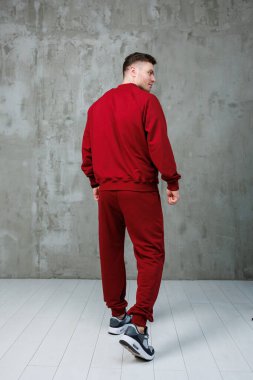 Canlı kırmızı eşofman giyen şık bir adam gururla çeşitli modern aktivite kıyafetleri sergiliyor.