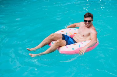 Şortlu şirin bir adam şişme bir yüzükle havuzda yüzüyor. Bekar bir adamın havuzunda yaz tatili.