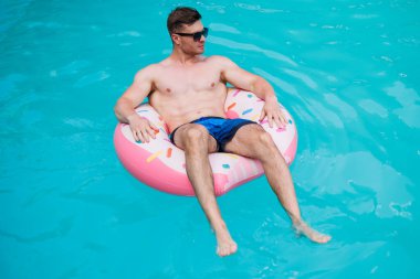 Şortlu şirin bir adam şişme bir yüzükle havuzda yüzüyor. Bekar bir adamın havuzunda yaz tatili.