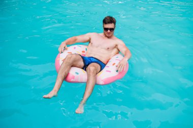 Şortlu şirin bir adam şişme bir yüzükle havuzda yüzüyor. Bekar bir adamın havuzunda yaz tatili.