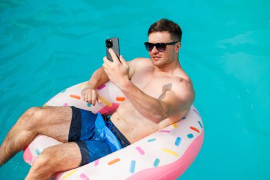 Şortlu şirin bir adam şişme bir yüzükle havuzda yüzüyor. Bekar bir adamın havuzunda yaz tatili.