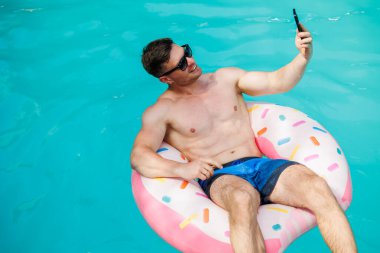 Şortlu şirin bir adam şişme bir yüzükle havuzda yüzüyor. Bekar bir adamın havuzunda yaz tatili.