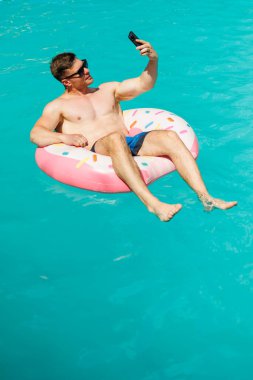 Şortlu şirin bir adam şişme bir yüzükle havuzda yüzüyor. Bekar bir adamın havuzunda yaz tatili.