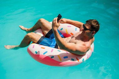 Şortlu şirin bir adam şişme bir yüzükle havuzda yüzüyor. Bekar bir adamın havuzunda yaz tatili.