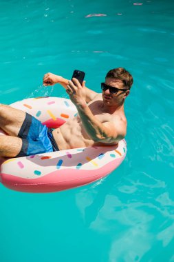 Şortlu şirin bir adam şişme bir yüzükle havuzda yüzüyor. Bekar bir adamın havuzunda yaz tatili.