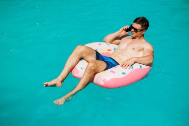 Şortlu şirin bir adam şişme bir yüzükle havuzda yüzüyor. Bekar bir adamın havuzunda yaz tatili.