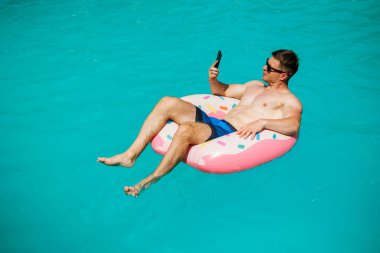 Şortlu şirin bir adam şişme bir yüzükle havuzda yüzüyor. Bekar bir adamın havuzunda yaz tatili.