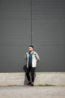 Bir adam ellerini arkasina yaslayarak duvara yaslaniyor ve rahat bir durus sergiliyor.