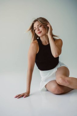 Bir kadın zarif bir şekilde oturur ve minimalist ve zarif bir ortamda modern bir moda anlayışı sergiler.