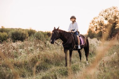 Genç bir binici, çarpıcı bir şekilde açık havada at sürerken huzurlu bir andan zevk alır.