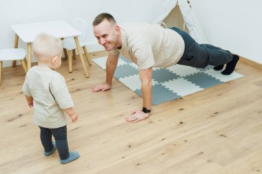 Bir baba evde, meraklı çocuğuyla şınav çekerek spor yapıyor. İzliyor, spor yapıyor ve bağ kuruyor..