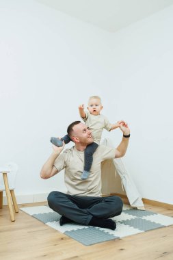 Neşeli bir baba ve oğlu birlikte oynuyorlar. Parlak, sıcak ve modern bir ortamda bağlarını kutluyorlar.