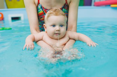 Neşeli bir bebek neşeli bir havuzda bir bakıcı ile eğlenceli ve çekici bir yüzme seansının keyfini çıkarıyor.