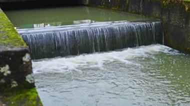 Sakin ve huzurlu bir su manzarası sert beton bir bariyerin üzerinden yavaşça geçiyor, yumuşak ve nazik dalgalanmalar yaratıyor.