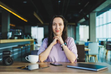 Bir kadın güvenli bir şekilde modern bir çalışma alanına oturur, kahve ve dijital cihazlarıyla yaratmaya hazırdır.