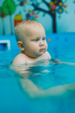 Havuzdaki çocuklar için yüzme dersleri. Bir bebek, bayan bir koçla havuzda yüzüyor..