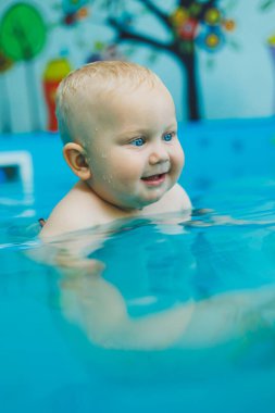 Havuzdaki çocuklar için yüzme dersleri. Bir bebek, bayan bir koçla havuzda yüzüyor..