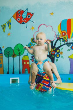 Çocuk havuzda koçla yüzmeyi öğreniyor. Çocuk havuzunda yüzmek. Kapalı havuzda koçu olan mutlu çocuk oynuyor ve eğleniyor..