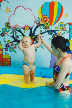 Çocuk havuzda koçla yüzmeyi öğreniyor. Çocuk havuzunda yüzmek. Kapalı havuzda koçu olan mutlu çocuk oynuyor ve eğleniyor..