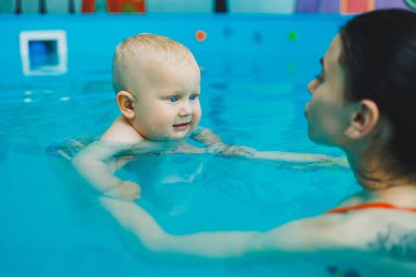 Havuzdaki çocuklar için yüzme dersleri. Bir bebek, bayan bir koçla havuzda yüzüyor..