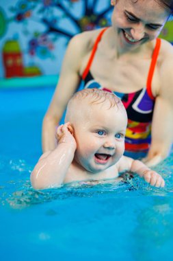 Bir antrenör havuzda bir bebekle ders veriyor. Çocuk antrenörle yüzmeyi öğrenir..