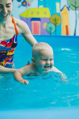 Küçük çocuklar için bir antrenörle havuzda yüzmek. Çocuk suda yüzmeyi öğrendi. Bir kadın eğitmenden mutlu bir çocuk. Bebeği olan sağlıklı ve sportif bir aile.