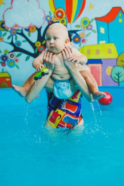 Bir eğitmenin gözetiminde yüzen bebekler için havuz. Havuzda çocuğu olan genç bir anne. Kadın kucağında bebek, suda eğleniyor.