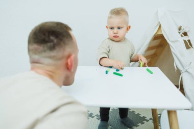 Bir yaşındaki küçük bir çocuk masada dururken plastik heykel yontuyor. Çocuk eğitici oyuncaklarla oynuyor..