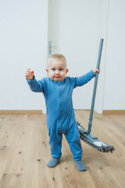 Neşeli küçük bir bebek neşeyle renkli bir temizlik aletini şık, aydınlık, davetkar bir odada tutuyor.