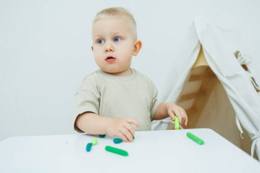 Bir yaşındaki küçük bir çocuk masada dururken plastik heykel yontuyor. Çocuk eğitici oyuncaklarla oynuyor..