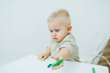 Bir yaşındaki küçük bir çocuk masada dururken plastik heykel yontuyor. Çocuk eğitici oyuncaklarla oynuyor..