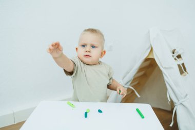 Bir yaşındaki küçük bir çocuk masada dururken plastik heykel yontuyor. Çocuk eğitici oyuncaklarla oynuyor..