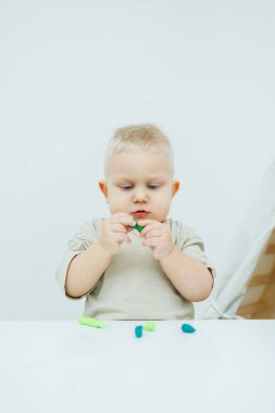Bir yaşındaki küçük bir çocuk masada dururken plastik heykel yontuyor. Çocuk eğitici oyuncaklarla oynuyor..