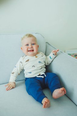 Sevimli bir erkek bebek mutlu bir şekilde gülümserken rahat ve rahat bir şekilde, neşeyle yumuşak bir koltukta oturuyor.