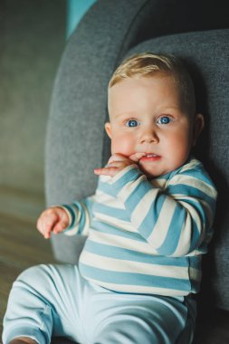 Parlak mavi gözlü, çizgili elbiseli sevimli bir bebek, rahat ve neşeli görünüyor.