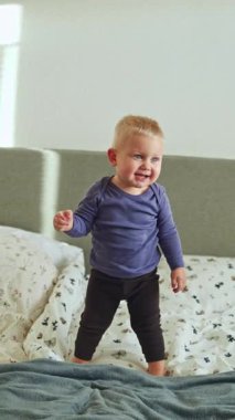 1 yaşında tatlı gülümseyen bir çocuk yatakta uzanıyor ve oyun oynuyor. Çocuk yatakta yatarken oyun oynuyor. Yatak odasında gülümseyen çocuk..