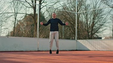 Eşofmanlı ve formalı genç bir adam basketbol sahasında spor yapıyor. Atletik vücutlu bir adam dışarıda spor yapıyor..