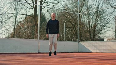 Eşofmanlı ve formalı genç bir adam basketbol sahasında spor yapıyor. Atletik vücutlu bir adam dışarıda spor yapıyor..