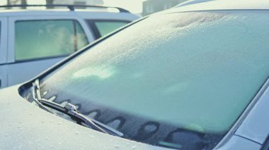 Donmuş bir arabanın ön camının yakından görüntüsü, güzel bir kış sabahının serin ve sakin atmosferini yakalıyor.