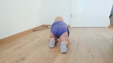 Sevimli bir bebek, ahşap bir zeminde mutlu bir şekilde emekler, merakla ve neşeyle çevrelerini keşfeder.