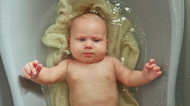 Bebek plastik bir küvette yatıyor ve banyo yapıyor. Bir çocuğu temiz suda yıkamak. Çocuk suda yatıyor..