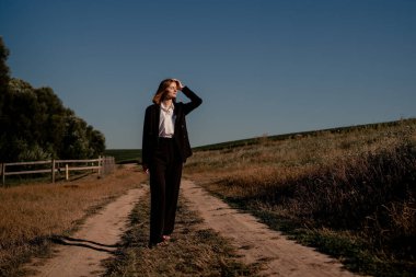 Gün batımında tarlada bir kadın. Büyük bir tarlada, gün batımında, siyah elbiseli mutlu bir kadın. Doğada batan güneşin altında yürümek