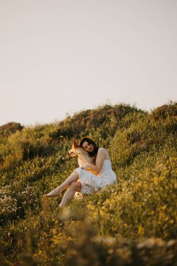 Bir kadın doğanın çarpıcı güzelliğinin keyfini çıkarırken sevgi dolu ve oyuncu köpeğiyle birlikte çimenli bir tepede.