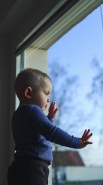 1 yaşında bir çocuk pencere pervazında dikiliyor ve pencereden dışarı bakıyor. Çocuk pencereden sokağa bakıyor..