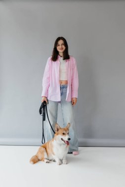 Şık giyimli bir kadın, modern, minimalist bir arkaplana karşı poz verirken sevimli Corgisini sergiliyor.